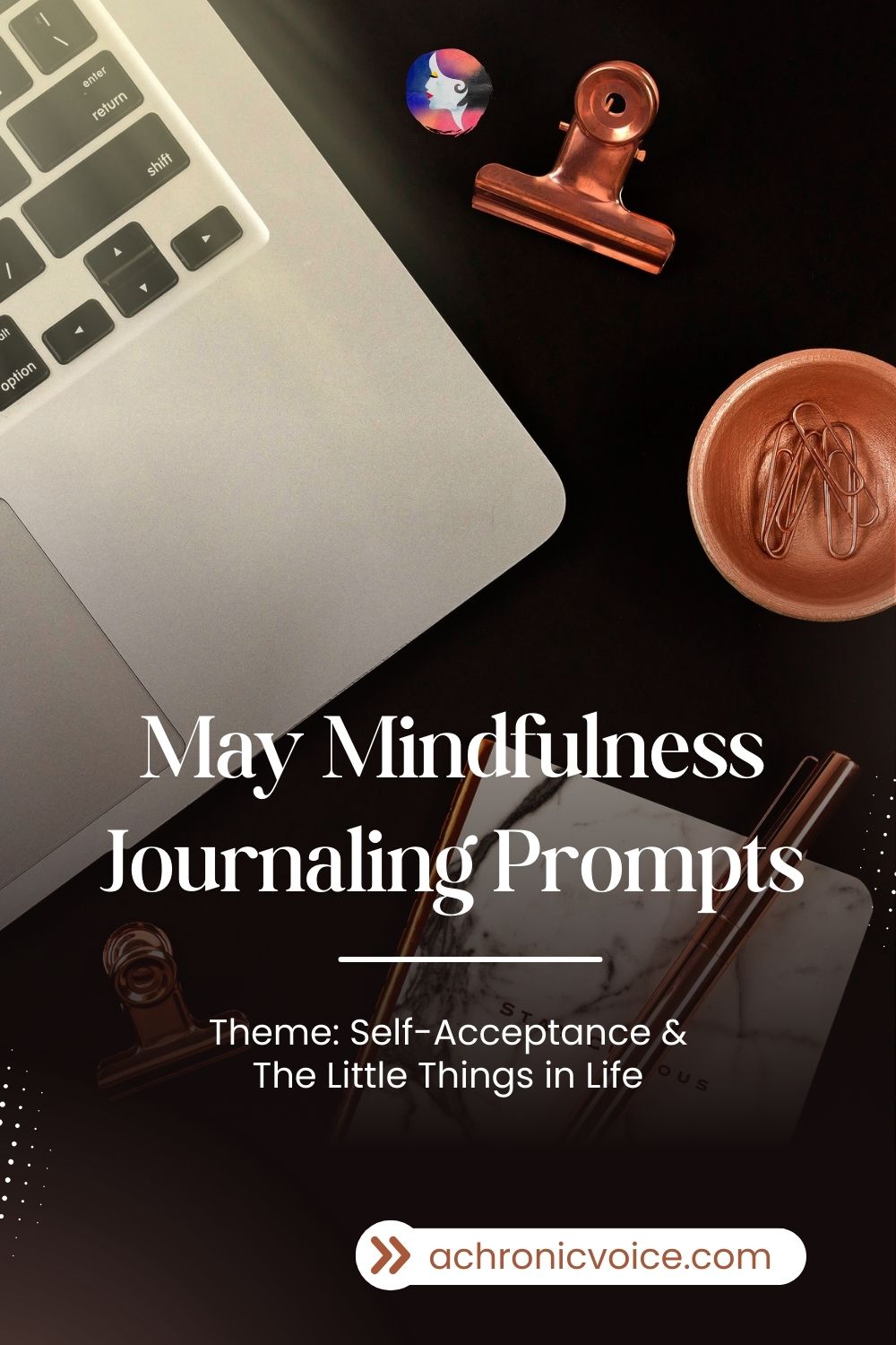May Mindfulness Journaling Prompts (Theme: Self-Acceptance and The Little Things in Life). The corner of a Mac laptop, a bronze bowl of paperclips, a shiny pen, and notebook with a marbled design cover can be seen laid flat against a black background.